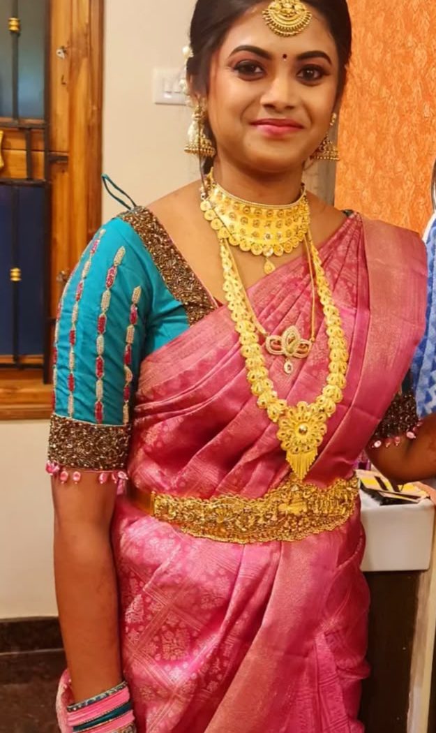 Bride in pink saree with teal blouse and gold choker